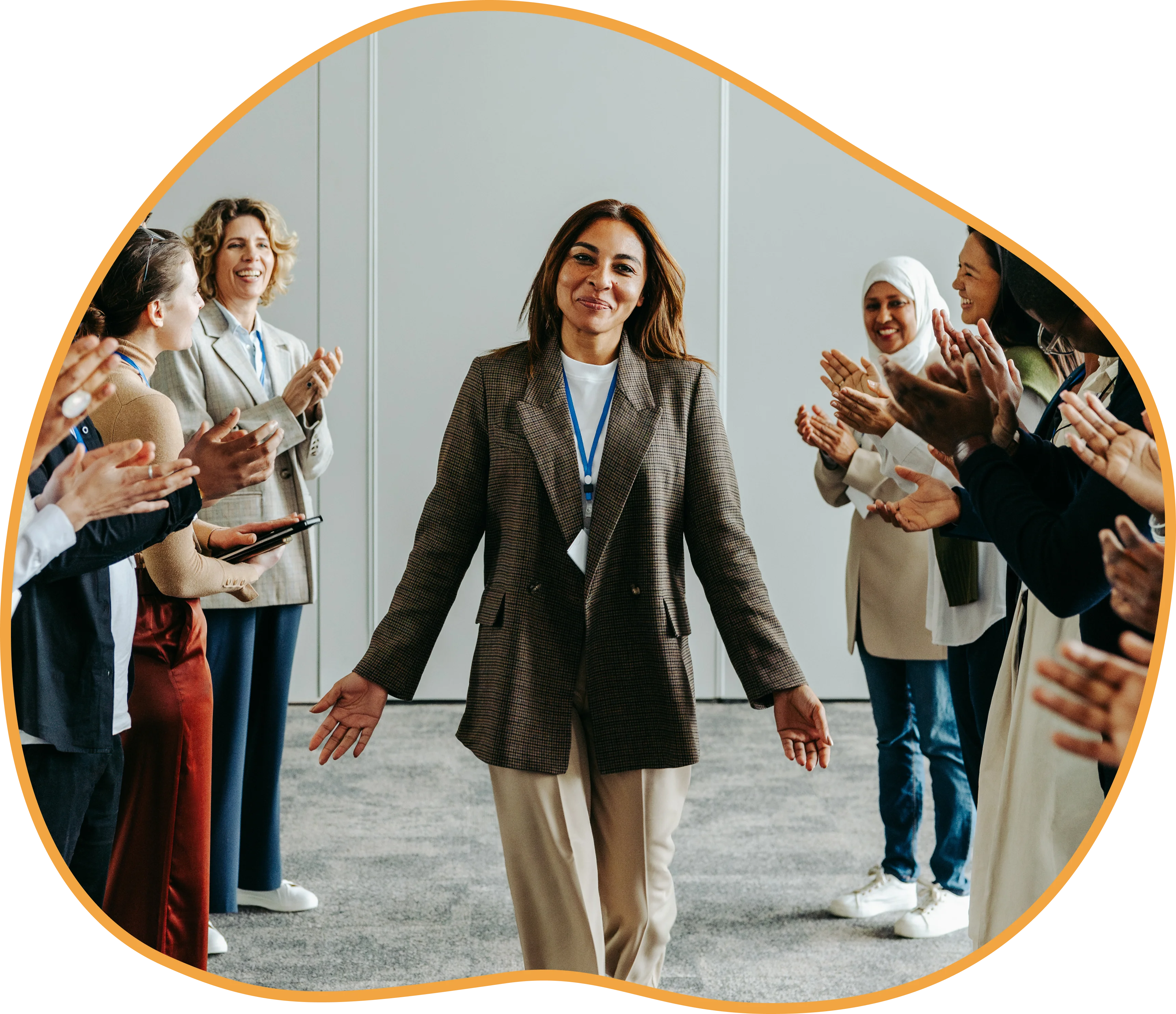 A woman in a blazer walks confidently down a hallway while being applauded by a group of people on both sides.